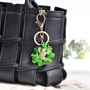 Enamel lotus leaf and rhinestone frog keychain pendant on a black woven texture bag