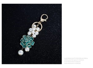 Détail du porte-clés fleur avec émail vert, perles et strass sur fond noir brillant