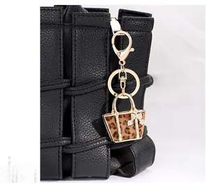 Macro shot of a leopard print handbag keychain with gold hardware on a black woven bag