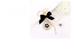 Detailed macro of golden perfume bottle keychain with black bow and white pearl chain
