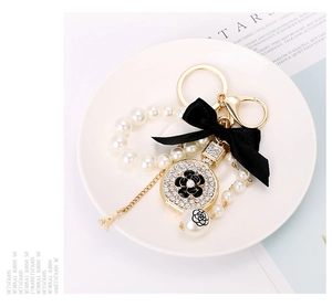 Detailed close-up of a gold perfume bottle keychain with camellia and pearls