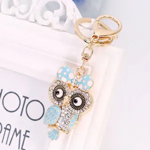 Portachiavi a forma di gufo dorato con smalto blu e strass su sfondo cornice bianca