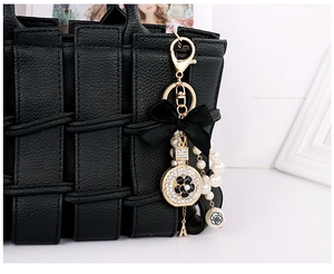 Detail of elegant gold keychain with black bow, faux pearls and camellia charm on handbag