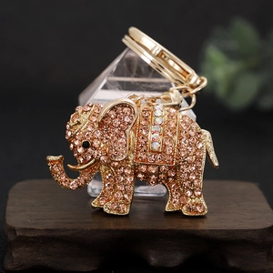 Elegant gold-tone elephant keychain with sparkling pink crystals on a wooden stand