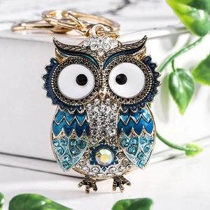 Golden owl keychain with blue enamel and rhinestones on marble surface