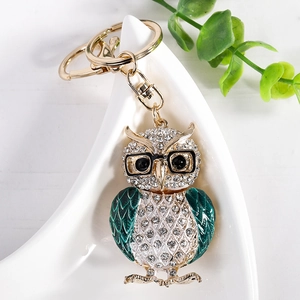Porte-clés hibou doré avec strass blancs et ailes vertes sur un plateau en céramique