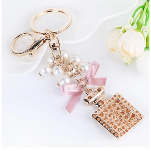 Dettaglio di un portachiavi a forma di flacone di profumo con fiocco rosa e perle
