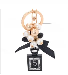 Dettaglio portachiavi con perla e fiocco con anello dorato e ciondolo boccetta di profumo nero
