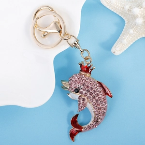 Pink rhinestone dolphin keychain with golden crown and red enamel on a blue background