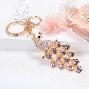 Llavero de pavo real brillante en oro con toques morados y cristales blancos
