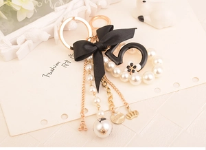 Close-up of pearl keychain with black number five, bow, and golden Eiffel Tower charm