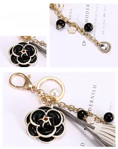Détail du porte-clés camélia avec chaîne en perles, pompon en cuir et fermoir mousqueton