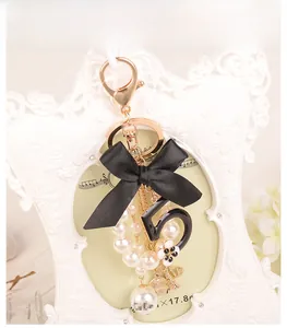 Detail of a pearl keychain featuring a black bow, number 5 charm, and heart pendant