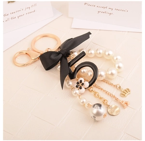 Detail of pearl keychain with black ribbon bow and gold tower charms on textured white surface