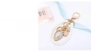 Close-up of pearl tulip keychain with opal pendant and golden clasp on pink background