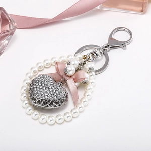 Exquisite rhinestone heart keychain with pearls and a pink silk bow on white background