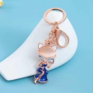 Pink cat eye fox keychain with blue enamel dress and crown on a blue background