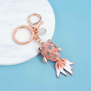Rose gold goldfish keychain with opal stones and pink enamel on a marble surface