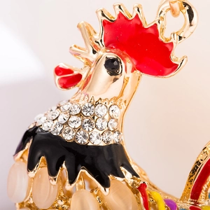 Détail macro d'un porte-clés coq en strass avec émail rouge et accents de pierre d'opale