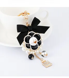 Detailed close-up of a camellia charm keychain with a bow and mini perfume bottle