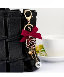 Detailed shot of camellia flower bag charm with burgundy bow and pearl beads on black bag