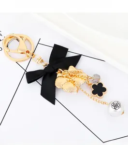 Detail of elegant black satin bow keychain with golden metal hook and camellia flower charm