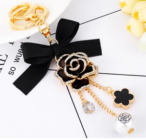 Detailed close-up of a floral keychain with black bow, crystal rose and clover charms