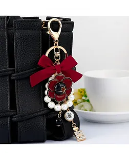 Detail of camellia floral charm with red bow and perfume bottle on black bag