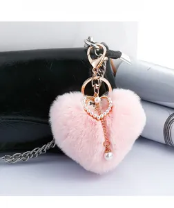 Detailed close-up of a pink plush heart keychain with pearls on a black handbag