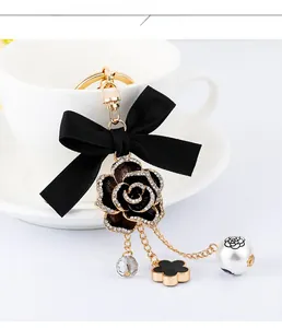 Detail of camellia keychain with black ribbon bow and pearl charms on white background
