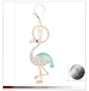 Détail d'un porte-clés flamant rose avec strass et émail à côté d'une pièce de monnaie