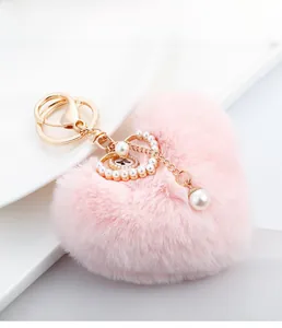 Detail of pink faux fur heart keychain with large pearl and gold hardware on white surface