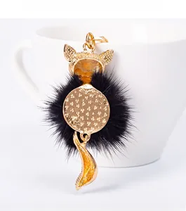 Detail of fox-shaped gold keychain with black faux fur ball and star-textured metal back
