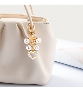 Detail of LOVE initial keychain with pearl heart pendant on a beige leather tote bag