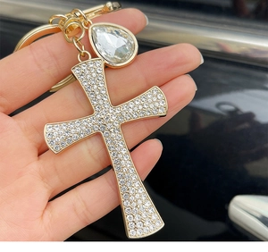 Close-up of golden cross keychain with shimmering white rhinestones and teardrop crystal