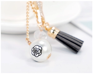 Detail view of pearl pendant with black floral pattern, leather tassel and gold chain