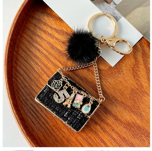 Detail of elegant black tweed mini bag keychain with golden charms and fur ball