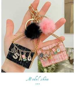 Close-up of pink tweed mini bag keychain with faux fur pom pom and gold charms