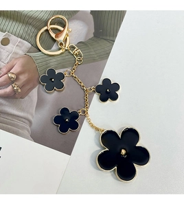 Detail of a golden alloy keychain with elegant black enamel five-petal flower pendants
