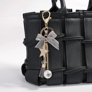 Star tassel keychain with grey bow and pearl hanging on a black woven leather bag