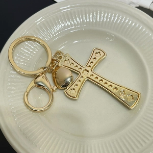 Golden cross keychain with embossed floral patterns and lobster clasp on white tray