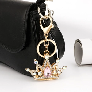 Golden crown keychain with pink gemstone and white crystals on a black leather handbag