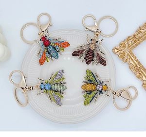 Close-up of four colorful crystal-encrusted bee keychains on a decorative white plate