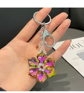 Detailed close-up of a gradient crystal flower keychain held by a hand over a magazine