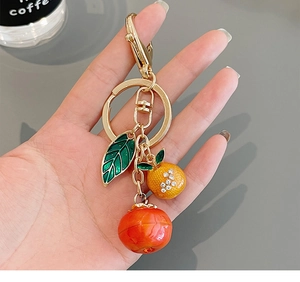 Detail of metal fruit keychain with enamel leaf, orange charm, and sparkling rhinestones