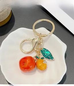Detailed close-up of persimmon and orange keychain with enamel leaf on a white tray