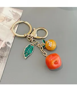 Detail of fruit keychain with gold ring, orange charm and green leaf on grey background