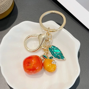 Golden creative fruit keychain with translucent persimmon and orange pendants in a tray