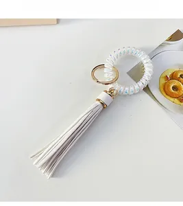 Detail of white PU leather tassel keychain with iridescent coil wristband and gold ring