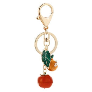 Golden keychain with orange and green leaf pendants and rhinestones on white background